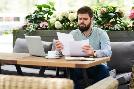 Frowning Businessman Reading Documents in Cafeの写真素材