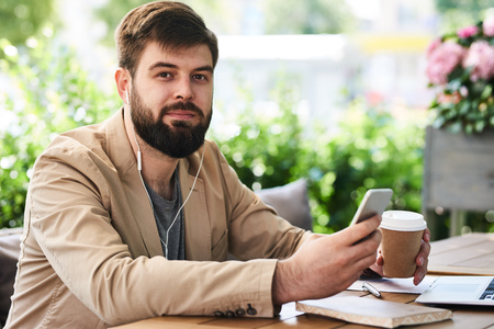 Smiling Bearded Man Using Smartphone in Cafeの写真素材