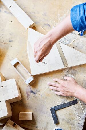 Directly above view of unrecognizable carpenter using compass to draw circle on wooden plank, surface of table covered with sawdustの写真素材