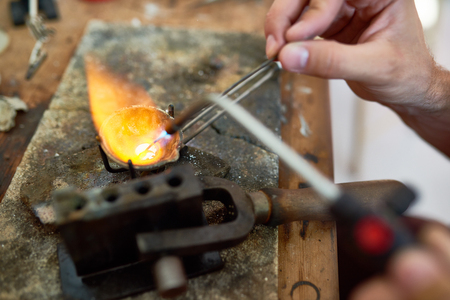 Closeup of unrecognizable jeweler melting precious metal on working table with different toolsの写真素材