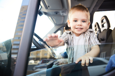 Portrait of cute little kid looking out of car window and smiling happily in sunlightの写真素材