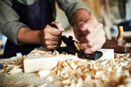 Closeup portrait of strong male hands shaving piece of wood with plane tool in carpenters workshop making furnitureの写真素材
