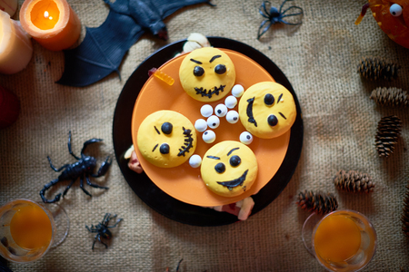High angle view of creative Halloween cake in orange and yellow colors decorated emoticon cookies and eyeball candies placed on burlap with drinks in glasses, cones toy spiders and batの写真素材