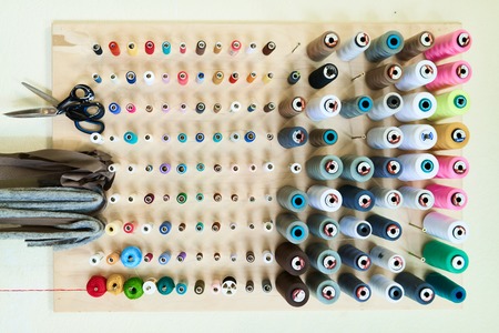 Directly above view on wooden holder used for colorful thread spools, scissors and shreds of cloth