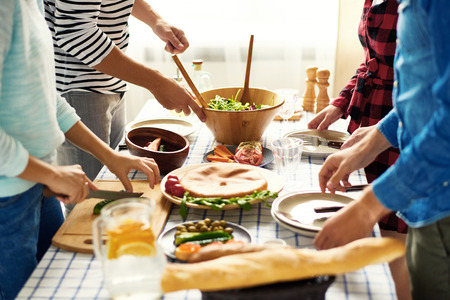 Mid-section group of young people preparing dinner for festive celebration standing at big table cutting vegetables for salad togetherの写真素材