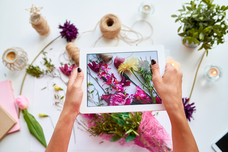 Top view closeup of female hands holding digital tablet and taking photo of floral decor composition for social mediaの写真素材