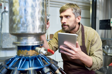 Busy male engineer adjusting brewery equipment at plantの写真素材