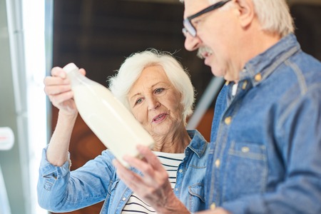 Portrait of modern senior couple choosing milk standing by dairy isle in supermarket while grocery shopping, copy spaceの写真素材
