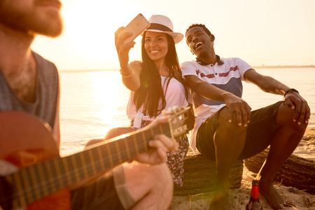Excited multiethnic tourists photographing singer on beachの写真素材