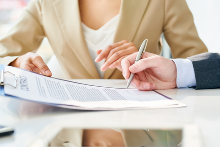 Side view close up of unrecognizable businessman signing contract during meeting with unrecognizable businesswoman sitting beside him explaining terms of dealの写真素材