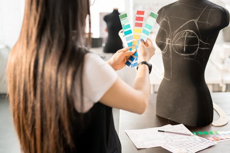 Back view portrait of focused Asian woman working in fashion design choosing color palette holding...