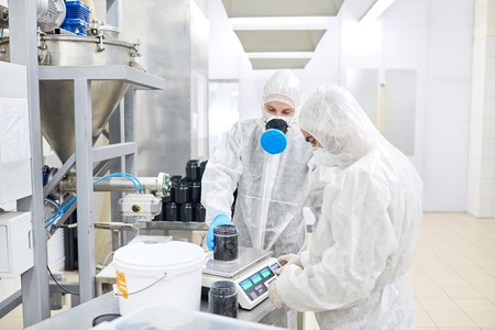 Factory workers weighing plastic container with product