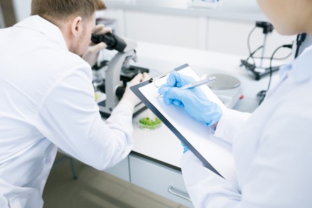 Scientists writing results of research under microscopeの写真素材