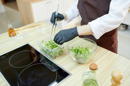 Closeup of unrecognizable female chef cooking salad standing at wooden table in restaurant kitchen, copy spaceの写真素材