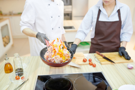 Closeup of modern professional chef mixing ingredients in frying pan while working in modern restaurant kitchen, copy spaceの写真素材
