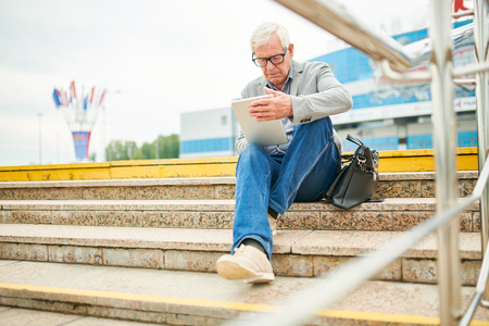 Elderly businessman using tablet on stepsの写真素材