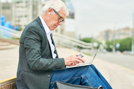 Aged businessman using laptop and listening to musicの写真素材