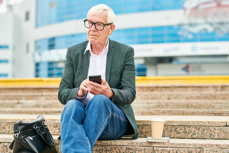 Senior businessman using smartphone and listening to music on stepsの写真素材