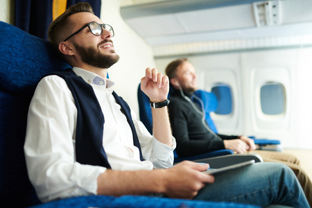 Side view portrait of handsome bearded man smiling happily while enjoying first class flight sitting in comfortable seat of modern plane, copy spaceの写真素材