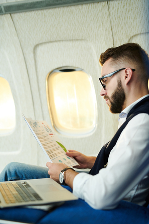Side view portrait  handsome businessman reading marketing reports while working in plane during long flight, copy spaceの写真素材