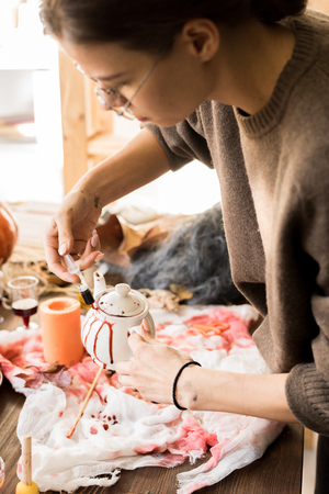 Woman using syringe while painting teapot with artificial bloodの写真素材
