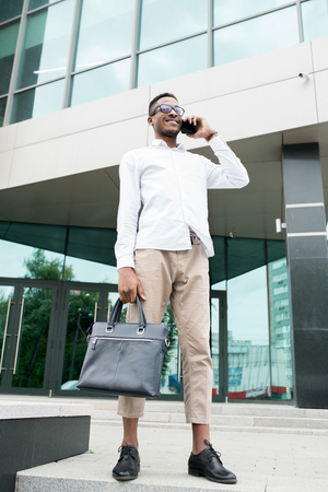 Cheerful handsome businessman walking and talking by phoneの写真素材