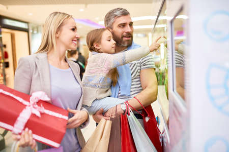 Girl with parents exploring shop window in mallの写真素材