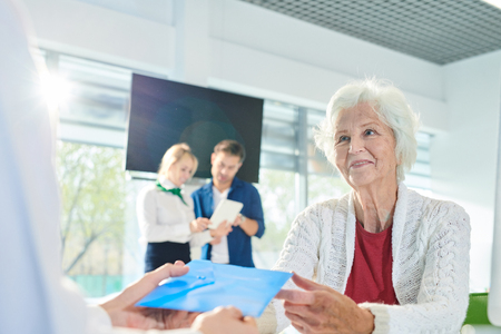 Positive senior lady receiving envelope with documents in bankの写真素材