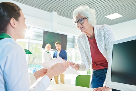 Outraged senior lady speaking loudly in travel agency officeの写真素材