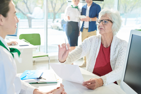 Displeased senior client reading contract in bank officeの写真素材