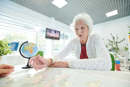 Shocked elderly lady pointing at map while talking to trip agentの写真素材