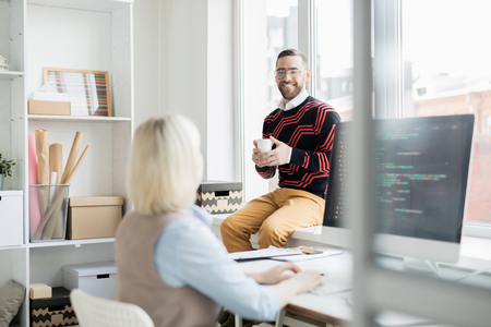 Cheerful office man drinking coffee while talking to coderの写真素材