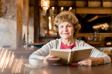 Smiling elderly lady reading favorite book in cafeの写真素材