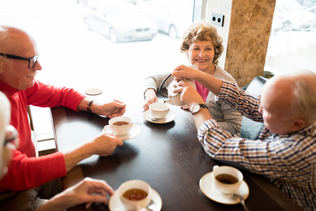 Positive senior friends drinking tea in cafeの写真素材