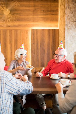 Cheerful senior lady giving cake with candle to friendの写真素材
