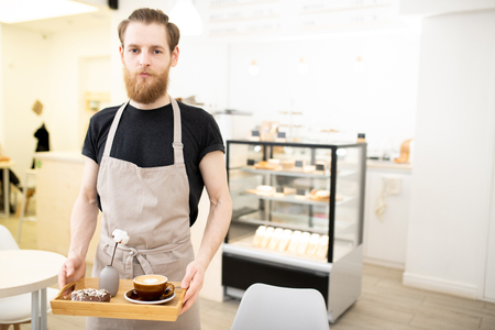 Handsome young barista carrying tray with cappuccinoの写真素材