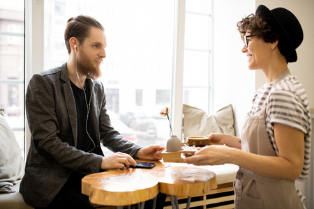 Positive waitress giving tray with coffee to customerの写真素材