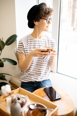 Pensive lady in hat drinking fresh-brewed coffeeの写真素材