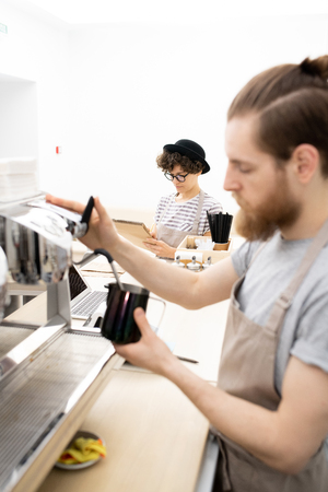 Waitress writing down orders while barista making coffeeの写真素材
