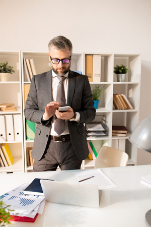 Bearded businessman in suit using smartphone in officeの写真素材