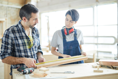 Carpenters checking measurement of wooden plankの写真素材