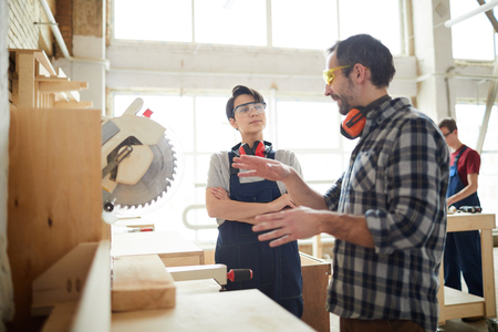 Carpenter giving advice to lady how to use circular sawの写真素材