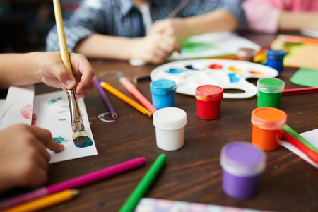 Closeup of children painting pictures, focus on art supplies paints, pencils and crayons, copy spaceの写真素材