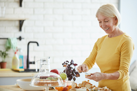 Positive woman preparing bruschetta in kitchenの写真素材