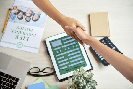 Life insurance agent shaking hand of client over office tableの写真素材