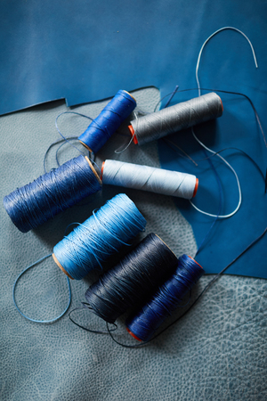 Top view closeup of several sewing spools lying on blue leather pattern in atelier or tannery, copy...
