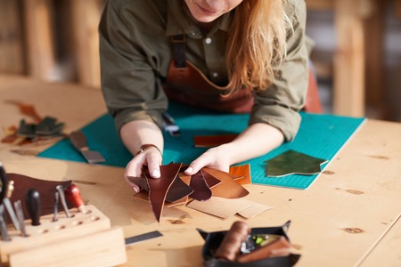 Warm toned close up of young  artisan holding leather pieces  in shoemaking  workshop, copy spaceの写真素材