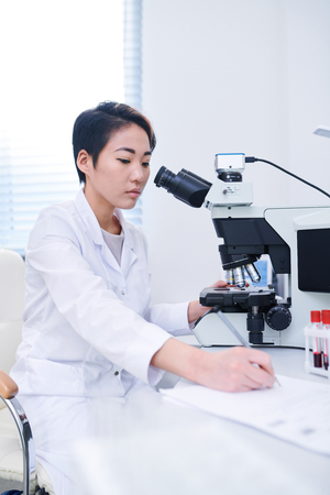 Asian biologist studying cells with microscopeの写真素材