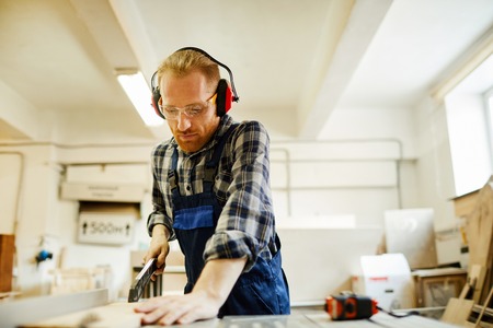 Waist up portrait of contemporary carpenter cutting wood while working in joinery, copy spaceの写真素材