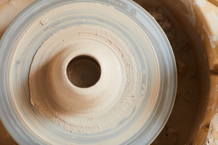 Directly above view of wet soft clay with hole in middle placed on dirty pottery wheel in ceramics studioの写真素材